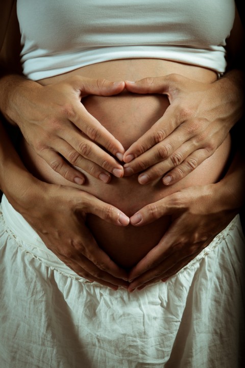 Sesión de fotos de embarazo, padres dibujan un corazón con las manos sobre la barriga